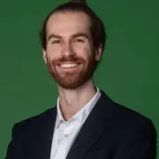 Foto von Philipp Schmitt in Hemd und Jacket,  wie er freundlich grinst, vor grünen Hintergrund,